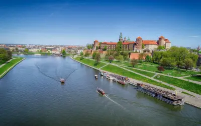 Widok na Wawel i Wisłę, najdłuższą rzekę w Polsce, z łodziami pływającymi po wodzie.