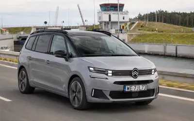Srebrny Citroen Picasso jedzie drogą obok kanału. W tle widoczna wieża kontrolna i podniesiony most.