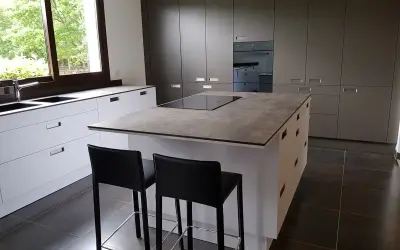 Cuisine moderne avec îlot central. On peut facilement faire le tour de cet îlot central pour accéder aux plans de travail et aux tabourets.
