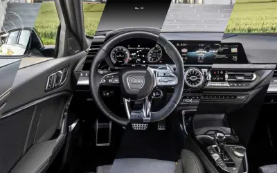 Interni moderni dell'Audi A3: volante sportivo, cruscotto digitale e console centrale con cambio automatico.