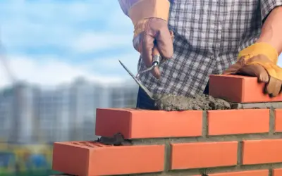 Murarz układa cegły, używając kielni do rozprowadzania zaprawy. Kluczowe są właściwe zaprawa murarska proporcje dla trwałej budowy.