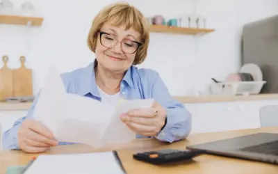 Uśmiechnięta starsza pani analizuje dokumenty, zastanawiając się, o ile wzrośnie emerytura po roku pracy na emeryturze.