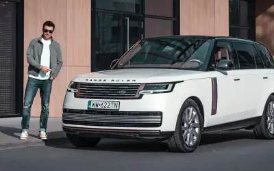 Elegancki mężczyzna obok białego Range Rovera. Sprawdź aktualną range rover cena i dowiedz się więcej o tym luksusowym SUV-ie.