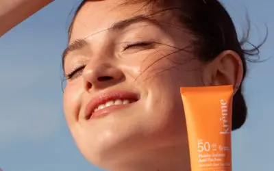 Une jeune femme rayonne sous le soleil, protégeant sa peau avec un fluide solaire. Un rappel : mettre de la crème solaire tous les jours pour une peau éclatante.