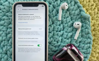 Jak sprawdzić pojemność baterii iPhone'a? Na ekranie widać 100% maksymalnej pojemności baterii, obok słuchawek AirPods.