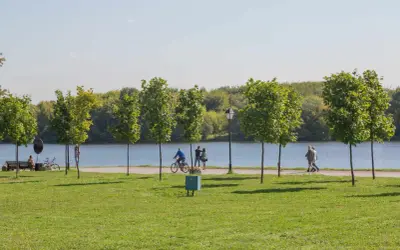 Spacer po zielonym brzegu zalewu nowohuckiego. Ludzie spacerują, jeżdżą na rowerze, ciesząc się słońcem i naturą.
