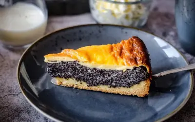 Ein Stück Mohn Schmand Kuchen mit goldbrauner Kruste und saftiger Mohnfüllung auf einem blauen Teller.