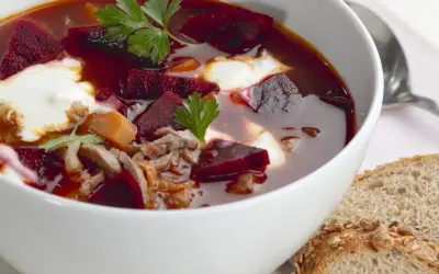 Herzhaftes Borschtsch-Rezept: Rote Bete, Fleisch und ein Klecks Sahne in einer Schüssel, dazu Brot.