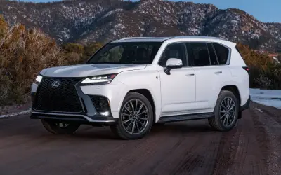 Biały Lexus LX 600 na drodze gruntowej, z ośnieżonymi górami w tle.