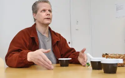 Kaj Linna gestikulerar vid ett bord med tre små mörka koppar framför sig.