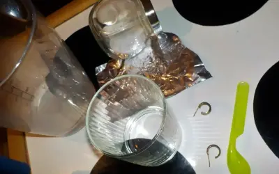 Przygotowania do czyszczenia złota folią aluminiową: szklanki, słoik, folia, łyżeczka i kolczyki.