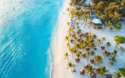 Rajska plaża na Zanzibarze w grudniu. Turkusowa woda, biały piasek, palmy i leżaki. Idealna pogoda na wakacje.