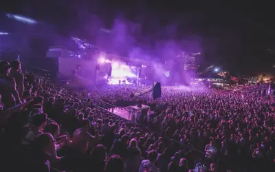 Tłum ludzi na nocnym koncercie, fioletowe światła i dym tworzą magiczną atmosferę. To niezapomniane u2 koncerty.
