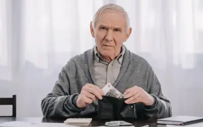 Zmartwiony starszy mężczyzna wkłada pieniądze do portfela, zastanawiając się, kiedy można przejść na wcześniejszą emeryturę.