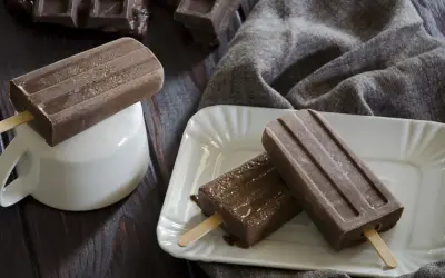 Tre ghiaccioli al cioccolato, uno su una tazza bianca, gli altri su un piatto, con pezzi di cioccolato sullo sfondo.