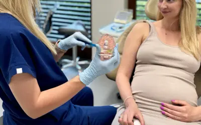 Dentystka pokazuje ciężarnej pacjentce model szczęki, omawiając higienę jamy ustnej. Piaskowanie zębów w ciąży jest bezpieczne i zalecane.