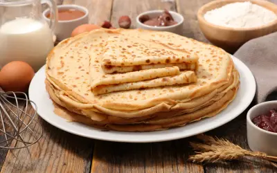 Una pila de crepes dorados, con ingredientes como leche, huevos y harina, evocan el origen de los crepes, un manjar sencillo y delicioso.