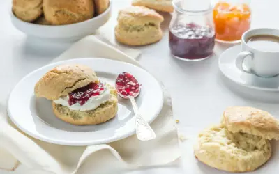 Ein Scone mit Clotted Cream und Marmelade, daneben eine Tasse Kaffee und weitere Scones.