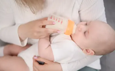 Mama karmi dziecko butelką z mlekiem. Na butelce widać miarkę, jak przy wycofanym mleku Bebilon.