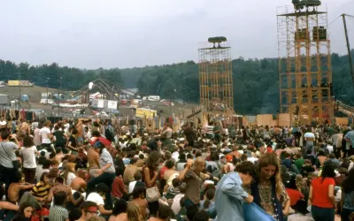 Tłum ludzi na festiwalu, widoczne wieże z głośnikami i scena w tle.