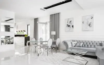 Eleganckie, nowoczesne wnętrze w stylu glamour. Błyszczące płytki, szara sofa i szklany stół tworzą luksusową atmosferę.