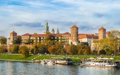 Wawel zwiedzanie z przewodnikiem. Widok na zamek i Wisłę z łodziami w jesiennej scenerii.