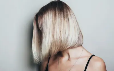 Kobieta z asymetryczną, blond fryzurą typu bob, z ciemniejszymi odrostami.