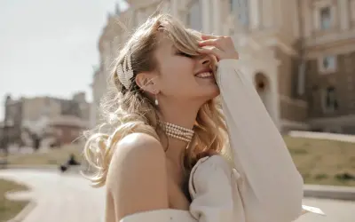 Uśmiechnięta blondynka w perłowej biżuterii, z perłową spinką we włosach. Masa perłowa znaczenie symbolizuje czystość i piękno.