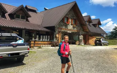 Ragazza con zaino e bastoncini da trekking davanti a un rifugio alpino, una delle tipiche malghe in Friuli.