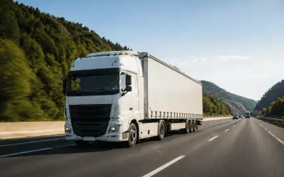 Un camion blanc roule sur une autoroute bordée d'arbres. Le conducteur utilise un chronotachygraphe numérique pour enregistrer son trajet.