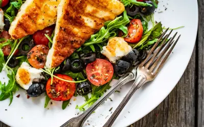 Pyszna sałatka z grillowanym halloumi, pomidorkami koktajlowymi i czarnymi oliwkami na rukoli. Idealna na lekki posiłek.
