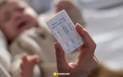 Dłoń trzyma test combo na COVID-19, grypę i RSV. W tle niewyraźne dziecko, być może z objawami RSV.