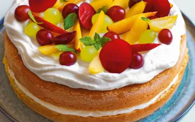 Torta con pan di spagna, panna montata e frutta fresca: uva, pesche e prugne. Un dolce estivo colorato e invitante.