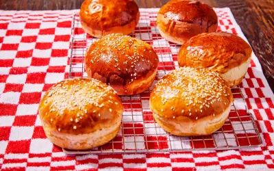 Petits pains à burger dorés et moelleux, certains parsemés de graines de sésame, sur une grille de refroidissement.