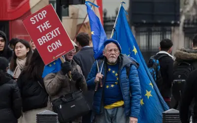 Protestujący w Wielkiej Brytanii z flagami UE i transparentem "Stop the Brexit Con".