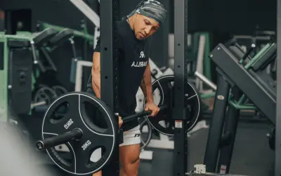 Mann mit Bandana macht schwere myo reps mit Langhantel im Fitnessstudio.
