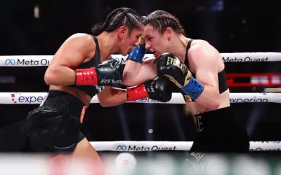 Two professional female boxers clash heads in the ring, their faces intense as they block punches.