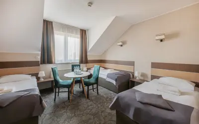 Pokój hotelowy z trzema łóżkami, stolikiem i krzesłami.