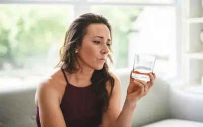 Kobieta zamyślona trzyma szklankę z bursztynowym płynem. Czy to izotek, czy alkohol?