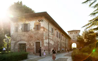 Passeggiata serale all'abbazia di Chiaravalle, con edifici storici in mattoni e un arco d'ingresso illuminato dal sole.