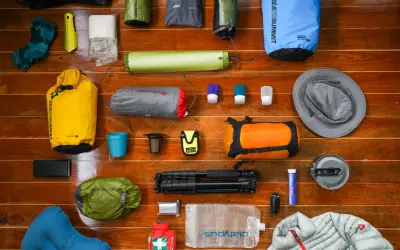 A collection of gear for a backpacking trip: dry bags, sleeping pad, socks, hat, first aid kit, water bladder, and more.