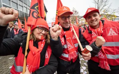 Drei Personen in roten Westen und Schals mit Gewerkschaftssymbolen, die Fahnen schwenken und die Faust ballen.