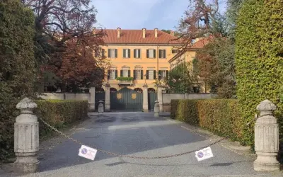 Ingresso di Villa San Martino ad Arcore, con cancello verde e alberi autunnali. Catena con cartelli di divieto di sosta blocca l'accesso.