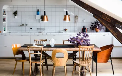 Une cuisine ouverte en L avec un îlot central en bois, des chaises vintage et des suspensions cuivrées. Une plante violette apporte une touche de couleur.