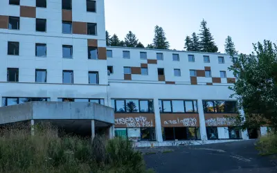 Bâtiment abandonné tagué, vestige d'urbex près du Puy de Dôme. La nature reprend ses droits, fenêtres brisées et végétation envahissante.