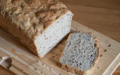 Chleb z lnem, świeżo upieczony, z jedną kromką obok, na drewnianej desce.