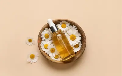 Flacon d'huile dorée entouré de marguerites dans un bol en bois. Le bisabolol, ingrédient clé, promet des bienfaits apaisants.
