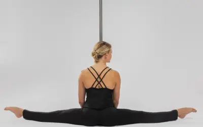 Kobieta w czarnym stroju siedzi w szpagacie przy rurze do pole dance.