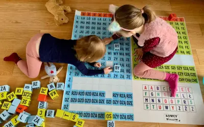 Dwie dziewczynki uczą się czytać, układając litery na planszy. Zabawa z literkami to świetny sposób, jak nauczyć dziecko czytać.