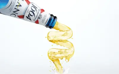 Piwo w niebieskiej butelce Kronenbourg 1664 leje się w fantazyjny sposób, tworząc złoty strumień.